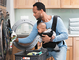 Dad carrying baby and loading the washing machine