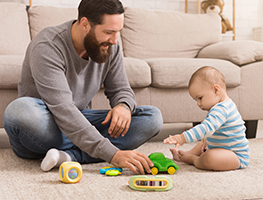 Man sitting on the floor next to a baby with toys