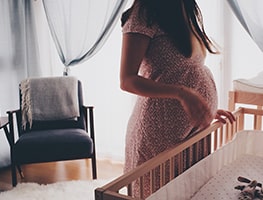 Pregnant woman standing beside a baby cot