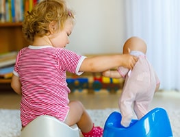 Toddler on a potty showing her doll how to use the potty