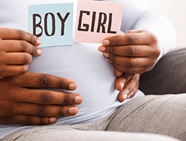 Pregnant mother and dad holding up boy and girl cards