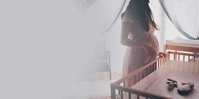 Pregnant woman standing beside a baby cot