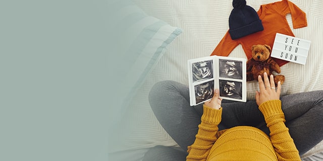 Woman looking at ultrasound photos and a teddy bear
