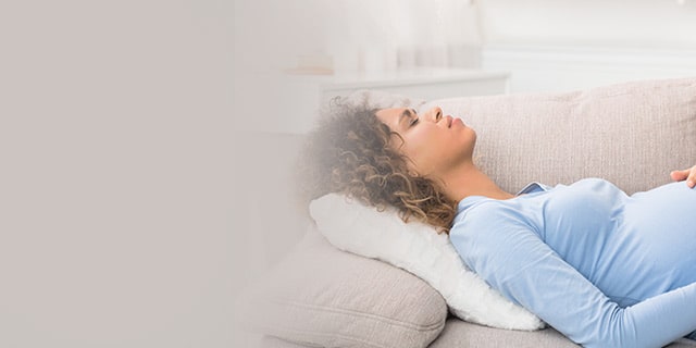 Pregnant woman in discomfort lying on a couch holding her belly